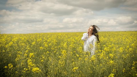 Cheerful girl of Caucasian appearance in rapeseed. Walks across the field in yellow flowers