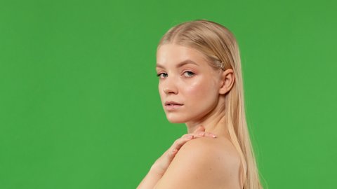 Beautiful blonde touching her neck while looking at camera standing on isolated green background. Concept of healthy clean skin