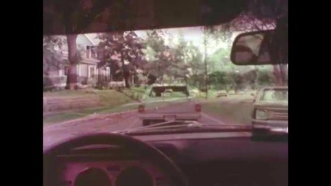 CIRCA 1980s - The driver of a small car is careful while passing a station wagon and, later, in the rain, headlights are illuminated, in 1983.