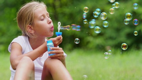 Girl playing with soap bubbles outdoors. The nine-year-old girl plays with soap bubbles in the summer garden. Slow motion.
