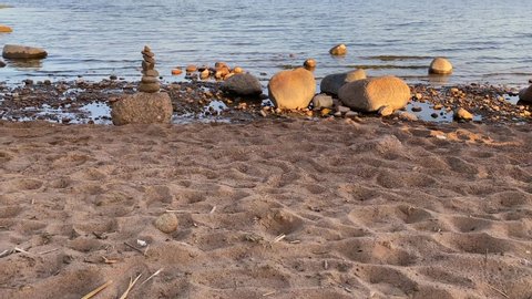 ST. PETERSBURG, RUSSIA - MAY 24, 2020: A guy with a girl walk along the beach past a stone pyramid of 7 stones against the background of the sea. Zen stone sculpture, a tower of river stones.