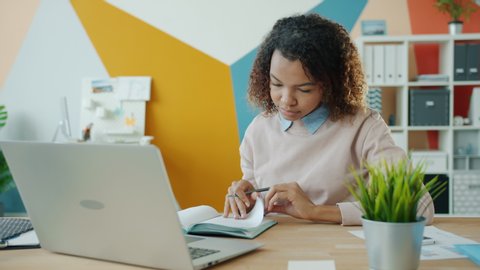 Serious young Afro-American woman is writing in notebook working in office alone concentrated on business information. People and workplace concept.