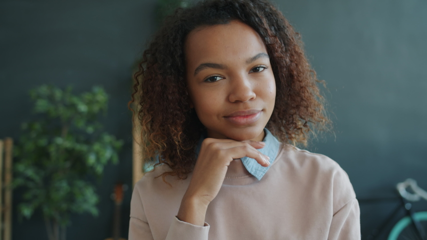 Portrait of attractive young Afro-American woman in casual clothing smiling indoors at home looking at camera. Happy youth, emotions and lifestyle concept.