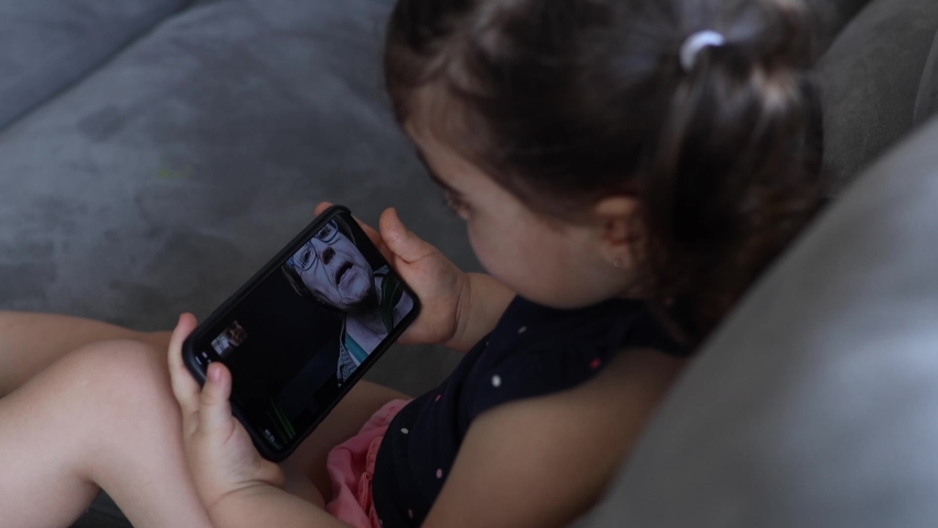 Little girl talking to their grandparents by videoconference through a smart phone from the living room | Shutterstock HD Video #1053998585
