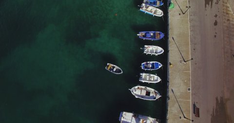 Aerial footage of small Greek harbor with sailboats and fisherman trawlers lined up at dock on a sunny day with no people. 2 different clips included in true C4k lossless Prores.