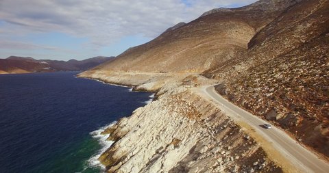 Aerial footage following single car driving up winding island highway. Blue waves crash on rocks in true C4k lossless Prores. 