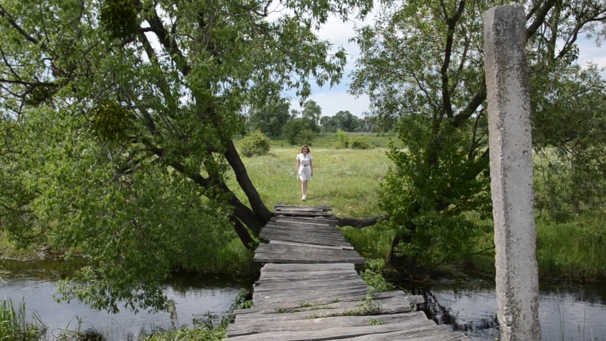 Young charming girl walks on an old wooden bridge over a small river | Shutterstock HD Video #1054013231