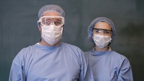 Male And Famele Doctor or Nurse Wearing Scrubs and Protective Mask and Goggles Banner. Smiling doctors look at the camera. 4K slow motion video.
