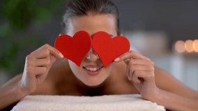 Woman enjoying body massage at spa club and covering eyes with hearts