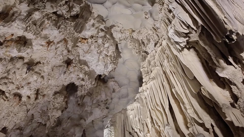 Cave limestone underground with white stalactites and stalagmites. Giant natural cavern amazing world illuminated by beautiful changing light. Panning rotation of the top in slow motion Royalty-Free Stock Footage #1054018862