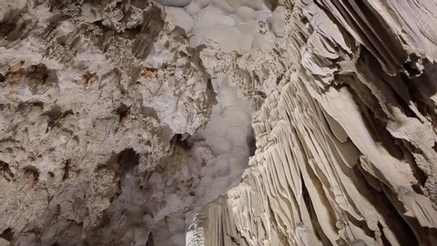 Cave limestone underground with white stalactites and stalagmites. Giant natural cavern amazing world illuminated by beautiful changing light. Panning rotation of the top in slow motion