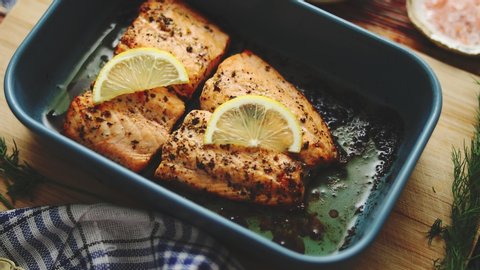 Roasted salmon in heat proof dish. With aromatic dill, lemon, salt and pepper on sides. Top View. Flat lay