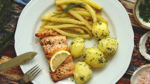 Fresh and tasty baked salmon served with young boiled potatoes and yellow bean. Sprinkled with aromatic dill. On a plate. Top View.
