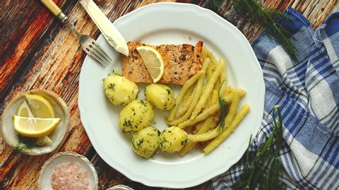 Fresh and tasty baked salmon served with young boiled potatoes and yellow bean. Sprinkled with aromatic dill. On a plate. Top View.