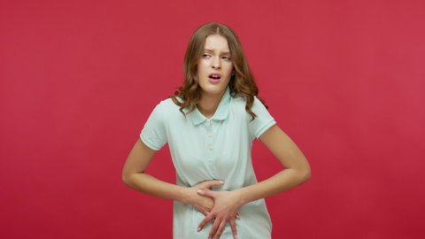 Gastrointestinal problems. Sick young woman in polo t-shirt suffering indigestion, abdominal pain, clutching stomach and feeling heartburn, pms cramps. indoor studio shot isolated on red background