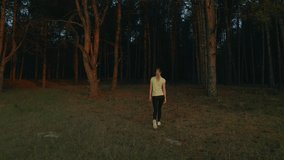 Young woman walking in beautiful forest at sunset, back view. Drone video recording