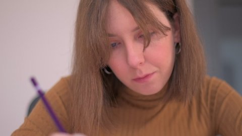 A slow motion tracking shot of young woman concentrating whilst sketching out a technical drawing at a desk