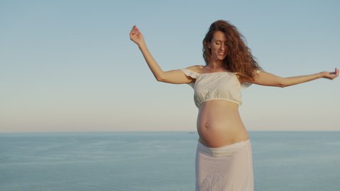 Pregnancy woman dancing emotionally having fun on the street against the background of the sea.