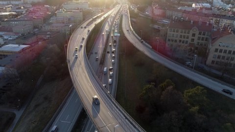 Aerial view of elevated highway traffic at sunset. Drone shot flying over junction, rush hour cars driving by. Urban transportation and air pollution background in 4K resolution