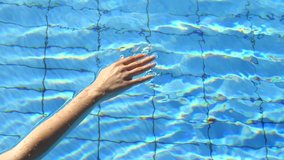 Female hand of girl leads through blue water of pool and creates waves, touches water. Summer holidays, relaxation, spa, vacation. Video screensaver for spa, relaxation. Slow motion video, meditation.
