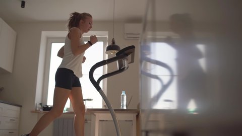 Woman running on running machine at home.Full length profile shot of a fit woman jogging on a treadmill in the kitchen.