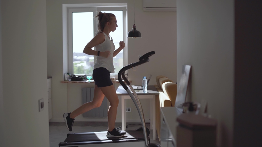 Woman running on running machine at home.Full length profile shot of a fit woman jogging on a treadmill in the kitchen.