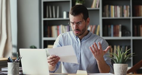 Stressed angry businessman opening envelope, reading banking credit loan refusal notification. Unhappy young man received bad news, irritated by mistake, feeling stressed about dismissal notice.