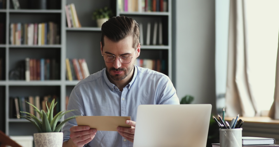 Curious smiling young man in glasses opening paper envelope, reading letter with good news. Happy handsome businessman received investment notification or banking loan approval or salary bonus. Royalty-Free Stock Footage #1054044065