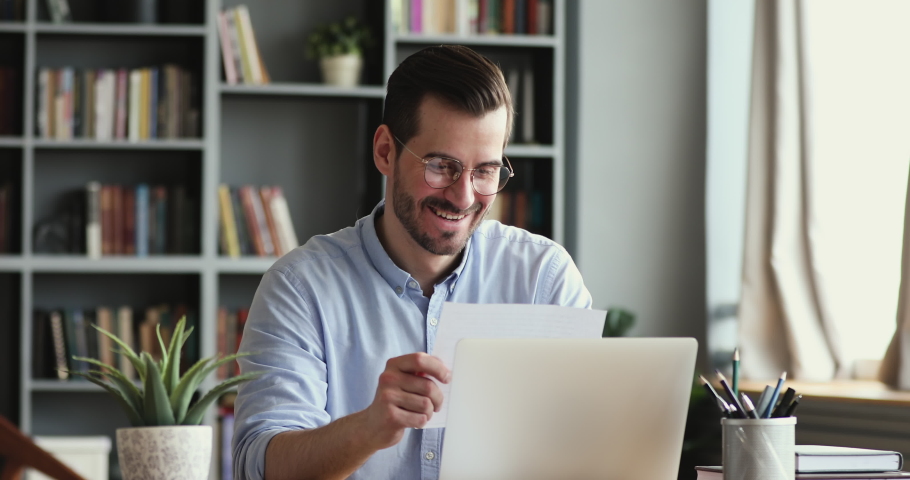 Curious smiling young man in glasses opening paper envelope, reading letter with good news. Happy handsome businessman received investment notification or banking loan approval or salary bonus. | Shutterstock HD Video #1054044065