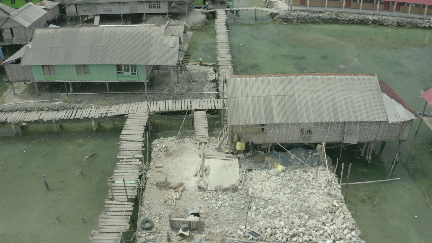 Aerial tilt up shot of stilt houses in village on sea, drone flying forward over structures against sky - Wakatobi Regency, Indonesia