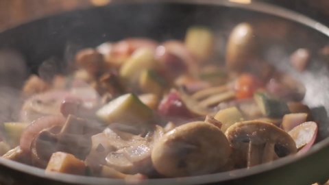 vegetables flying into the pan in slow motion. Onions, broccoli, mushrooms, champignons, tomatoes, zucchini. Healthy vegetarian food. Cooking on fire