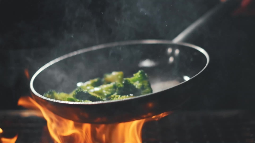 Cook fries broccoli in a pan. Flying vegetables. Cooking on fire and coal. Slow motion Royalty-Free Stock Footage #1054045100