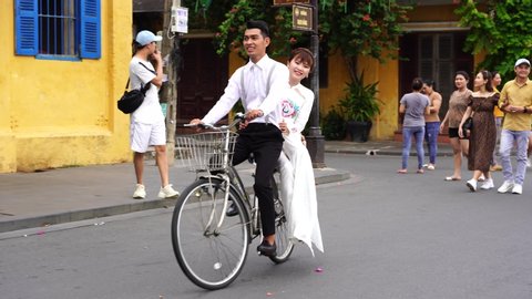 Hoi An, Vietnam - june 05, 2020 : Beautiful Vietnamese girl and guy rides a bike along the street of the old town Hoi An, Vietnam