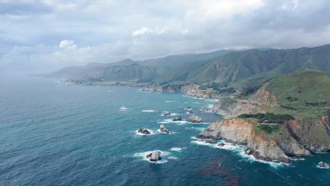Stunning aerial view over the rocky ocean coast. Beautiful ocean water of various shades of blue meets the rocky shore. Most scenic stretch of undeveloped coastline in USA, known as Big Sur. 4K