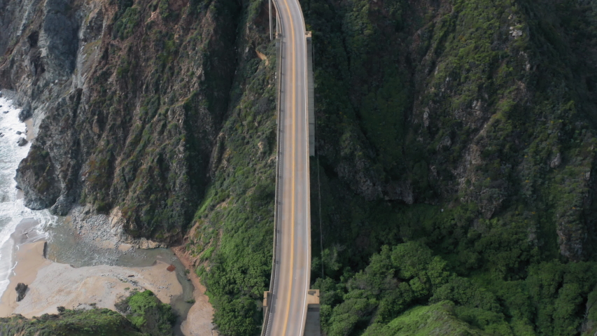 Aerial view of the picturesque arch bridge standing over the canyon among the beautiful hills covered with green grass. Cars move across the bridge. Famous landmark of USA under the cloudy sky. 4K