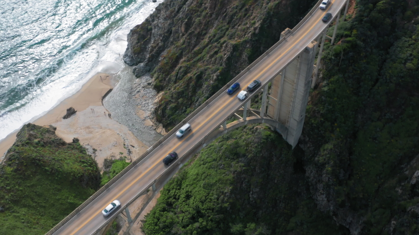 Aerial topdown survey over the high narrow concrete construction of Bixby Bridge crossing the creek on the coastline of Pacific Ocean and being a part of scenic coastal route. 4K Royalty-Free Stock Footage #1054048859
