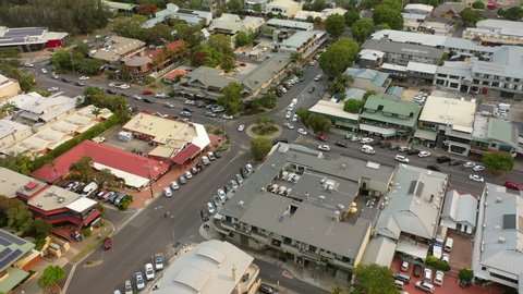 Aerial tilt down shot of vehicles at roundabout amidst buildings in city, drone flying over structures - Byron Bay, Australia