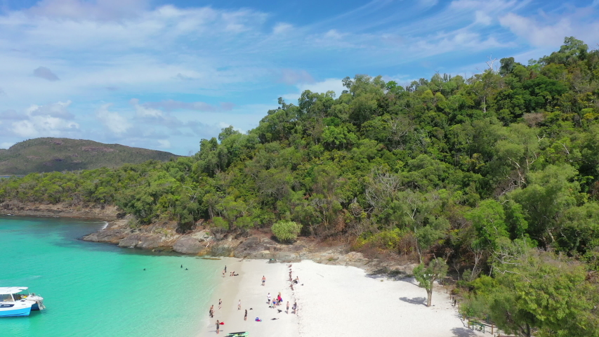 Aerial panning shot of people by trees at beach against sky, drone flying forward over shore on sunny day - Whitehaven Beach, Australia