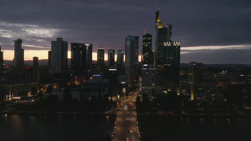 AERIAL: Wide Establishing Shot of Frankfurt am Main, Germany Skyline at Night over Main River and Bridge with Little Car traffic