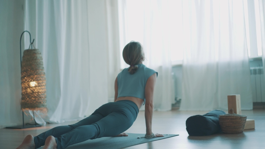 Middle-aged blonde woman practice yoga sun salutation
Body care morning routine at cozy interior room indoor 
Down and up facing dog pose asana for body care, healthy spine and productive day | Shutterstock HD Video #1054053239
