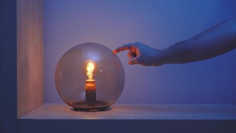 Faceless person turning on and after few seconds turning off with her finger creative table lamp with dark glass dome on in blue room in evening