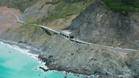 Incredible aerial view on the light blue deep ocean waters along green mountains of the Californian coastline. The Narrow tunnel on the Pacific highway at the Big Sur Park area. 4K drone video, USA.