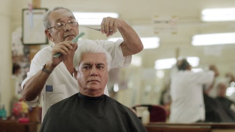Active senior people, man as client getting an haircut by elderly barber at work in old fashion male beauty shop or hair salon