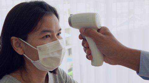 doctor using infrared thermometer to measure temperature of sick asian woman patient who visited at clinic in hospital. healthcare and medical concept