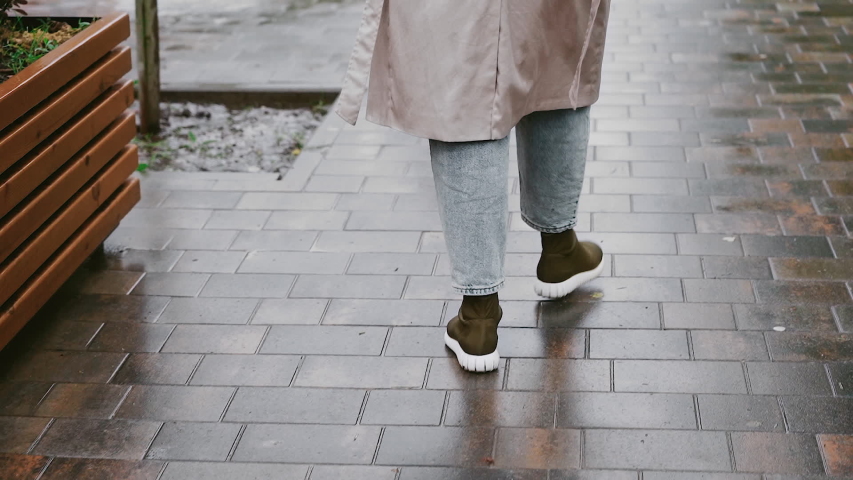 A young, attractive woman with an open umbrella strolls through a rainy the street The girl looks very happy walking in nature. tracking shot. in slow motion.