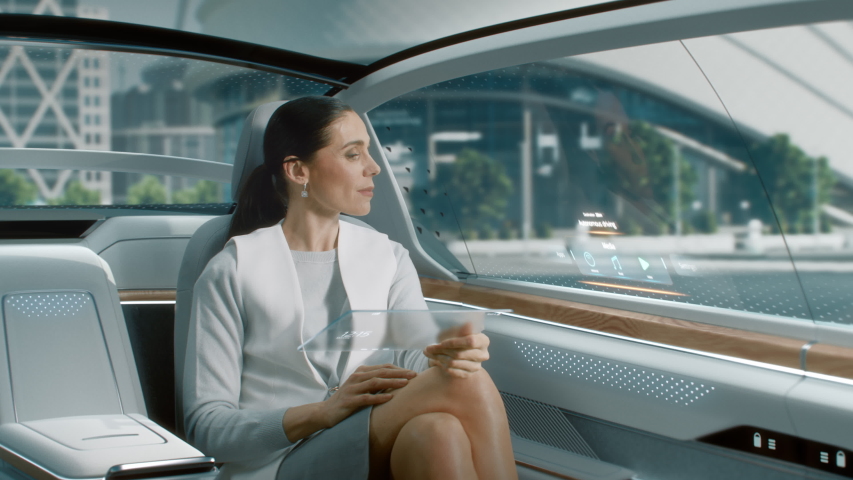 Futuristic Concept: Attractive Stylish Female Reading News on a Futuristic Transparent Tablet Computer with Augmented Reality Interface while Sitting on a Backseat of Autonomous Self-Driving Car Royalty-Free Stock Footage #1054062326
