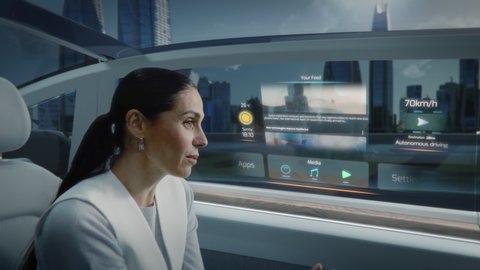 Futuristic Concept: Zoom Out View of an Attractive Female Reading the News on a Futuristic Augmented Reality Interface while Talking to Another Passenger. Riding in an Autonomous Self-Driving Car.