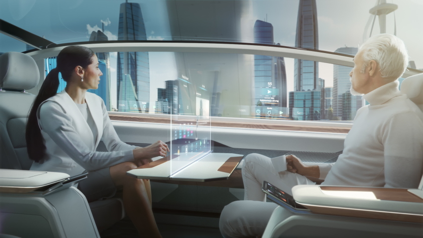 Futuristic Concept: Business Meeting Between Senior Male and Stylish Female inside a Futuristic Driverless Autonomous Car with Augmented Reality Presentation Interface. Self-Driving on City Streets Royalty-Free Stock Footage #1054062335