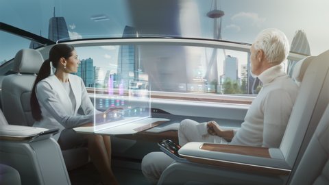 Futuristic Concept: Business Meeting Between Senior Male and Stylish Female inside a Futuristic Driverless Autonomous Car with Augmented Reality Presentation Interface. Self-Driving on City Streets