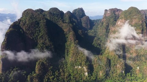 Aerial view of early morning clouds around huge, jungle covered limestone cliffs and mountains in a remote area